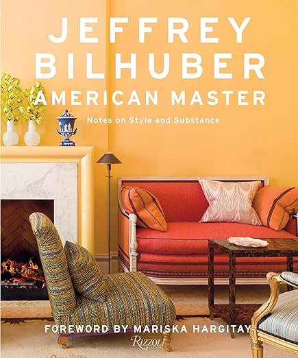 The cover of "Jeffrey Bilhuber American Master," published by Random House, features a stylish living room that exemplifies exquisite interior design with an orange wall, a striped armchair, a red sofa, a white marble fireplace, and a small table. The title is prominently displayed in large white text, with a foreword by Mariska Hargitay.