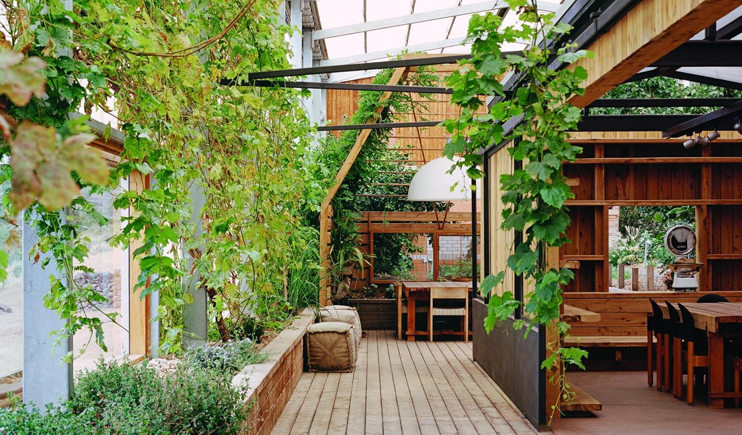 Discover nature-inspired decor with "Outside In: Thoughtful Interiors" by Random House, featuring cozy wood floors, green vines on trellises, cushioned benches, and sunlit tables beneath a glass roof for beautiful homes.