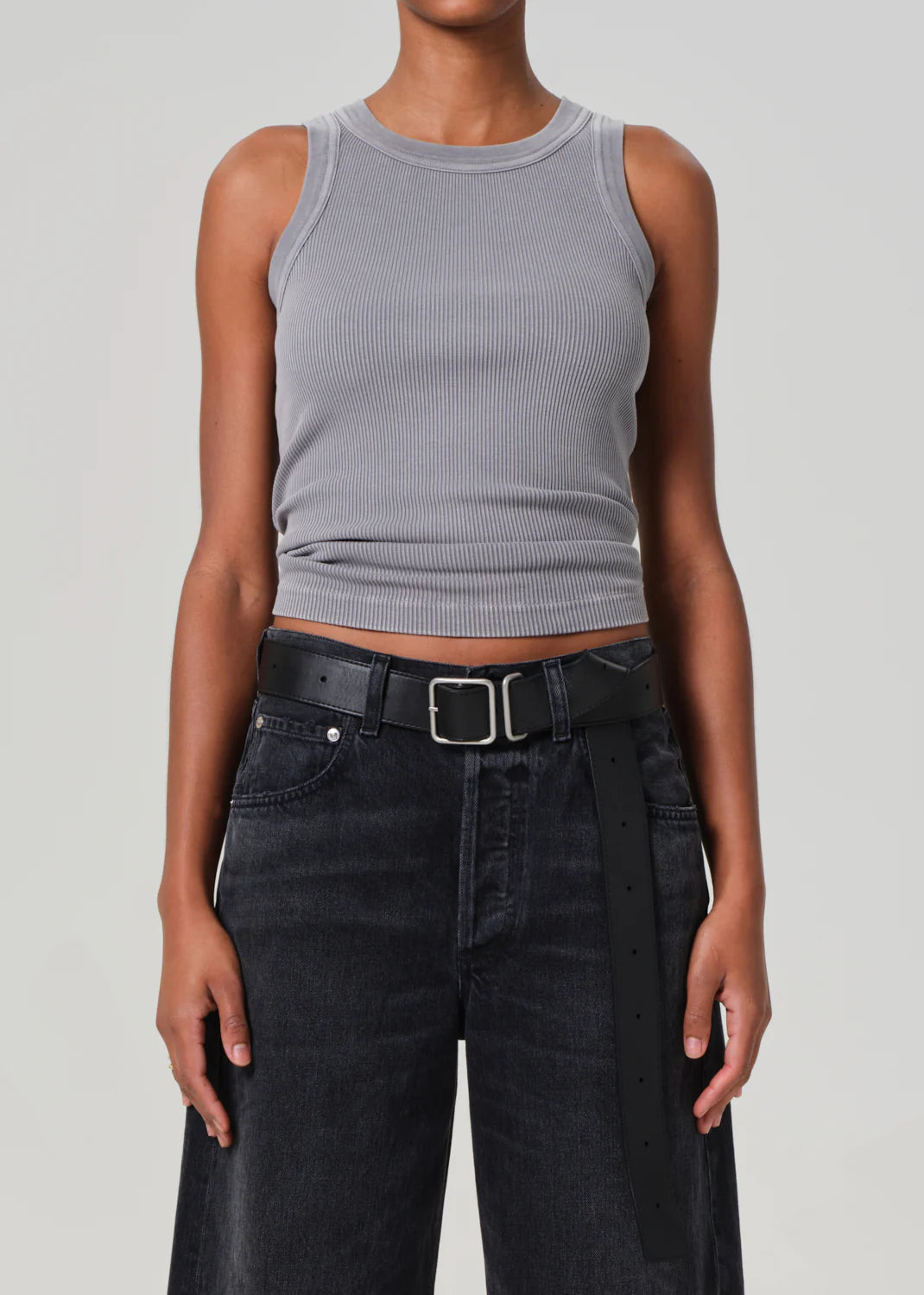 Wearing the Isabel Rib Tank by Citizens Of Humanity/AGOLDE, a person layers this gray racerback with high-waisted black jeans and a sleek black belt. Their arms rest relaxed by their sides against a neutral backdrop.