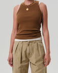 Wearing the Isabel Rib Tank F25 by Citizens Of Humanity/AGOLDE, layered over a white tank top with khaki pleated pants and gold necklaces, this person stands against a plain light background.