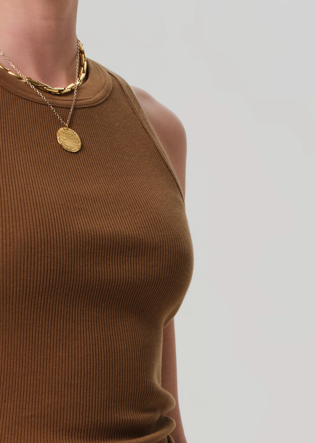 A person wears the Isabel Rib Tank F25 by Citizens Of Humanity/AGOLDE, a brown ribbed cotton sleeveless top with a high neckline, paired with two layered gold necklaces against a plain light background.