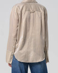 A person is wearing the Citizens Of Humanity/AGOLDE Camilia Shirt—a loose-fitting, beige and white striped cotton silk blend blouse with buttoned cuffs—paired with blue jeans. Photo shows the back view against a plain background.