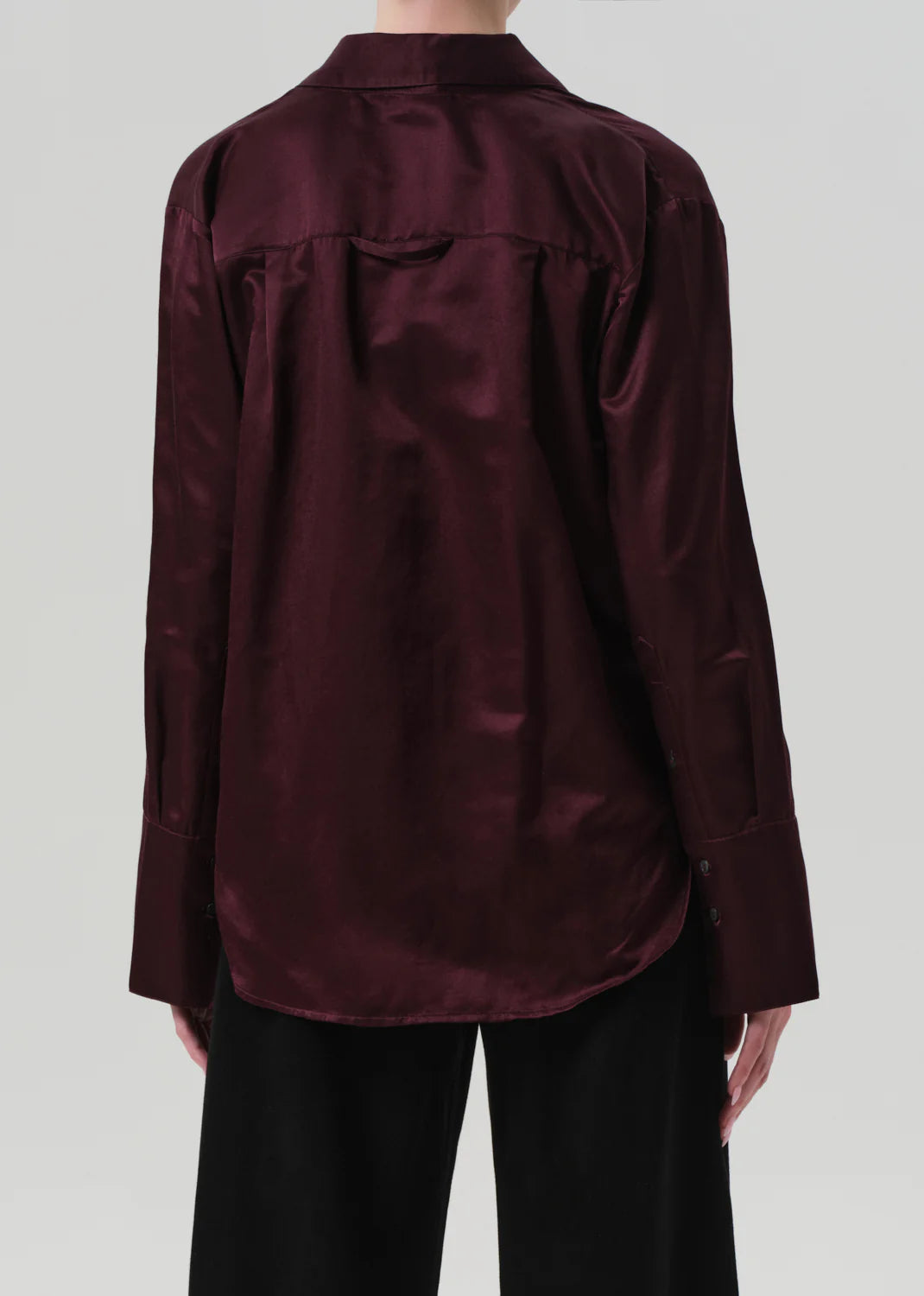 A person is seen from the back wearing the Citizens Of Humanity/AGOLDE Camilia Shirt, a burgundy long sleeve button-front blouse, styled with loose black pants against a plain light background.