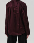 A person is seen from the back wearing the Citizens Of Humanity/AGOLDE Camilia Shirt, a burgundy long sleeve button-front blouse, styled with loose black pants against a plain light background.