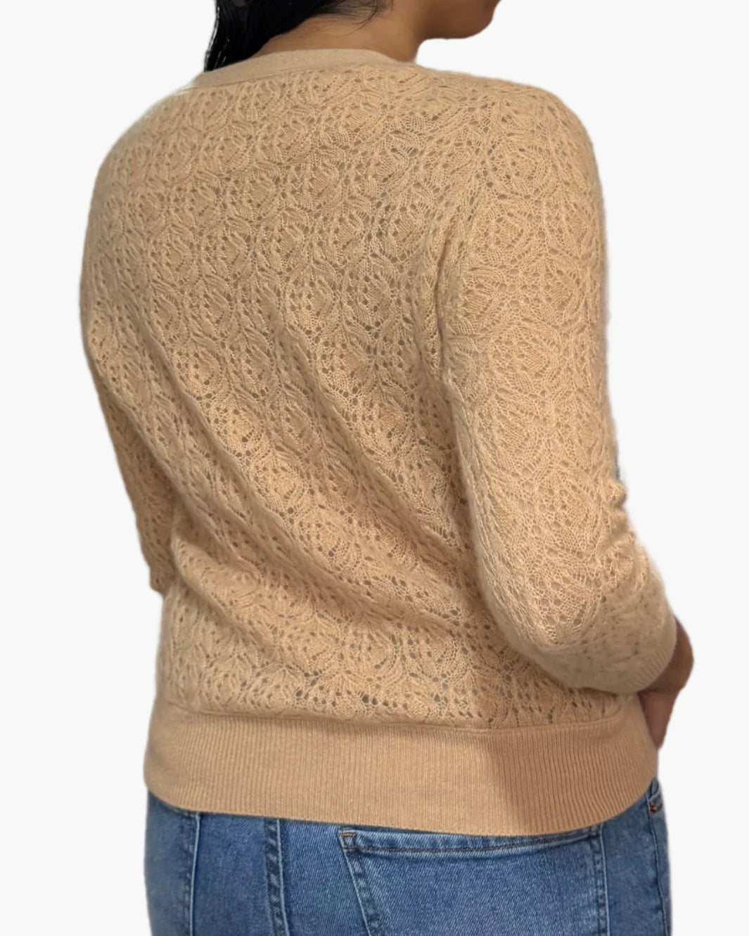 A woman is seen from behind wearing the Brazeau Tricot Lace Patch Cardigan, a beige long-sleeve knit with a leaf-like pattern, paired with blue jeans against a white background.