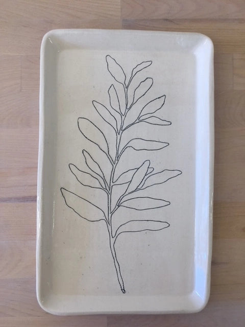 The Faire CSF Tray is a rectangular ceramic tray with rounded corners, showcasing a simple black line sage branch design on a cream background, displayed on a light wooden surface.