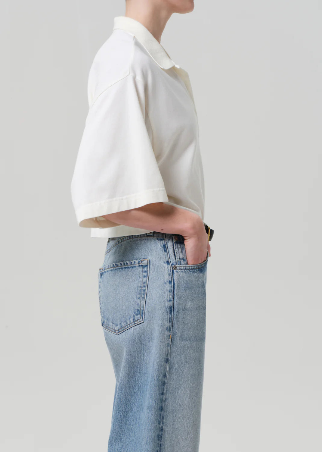 A person stands in profile with one hand in the pocket of light blue jeans, wearing the Citizens Of Humanity/AGOLDE Lowen Polo Shirt in breathable pique fabric, set against a plain light background.