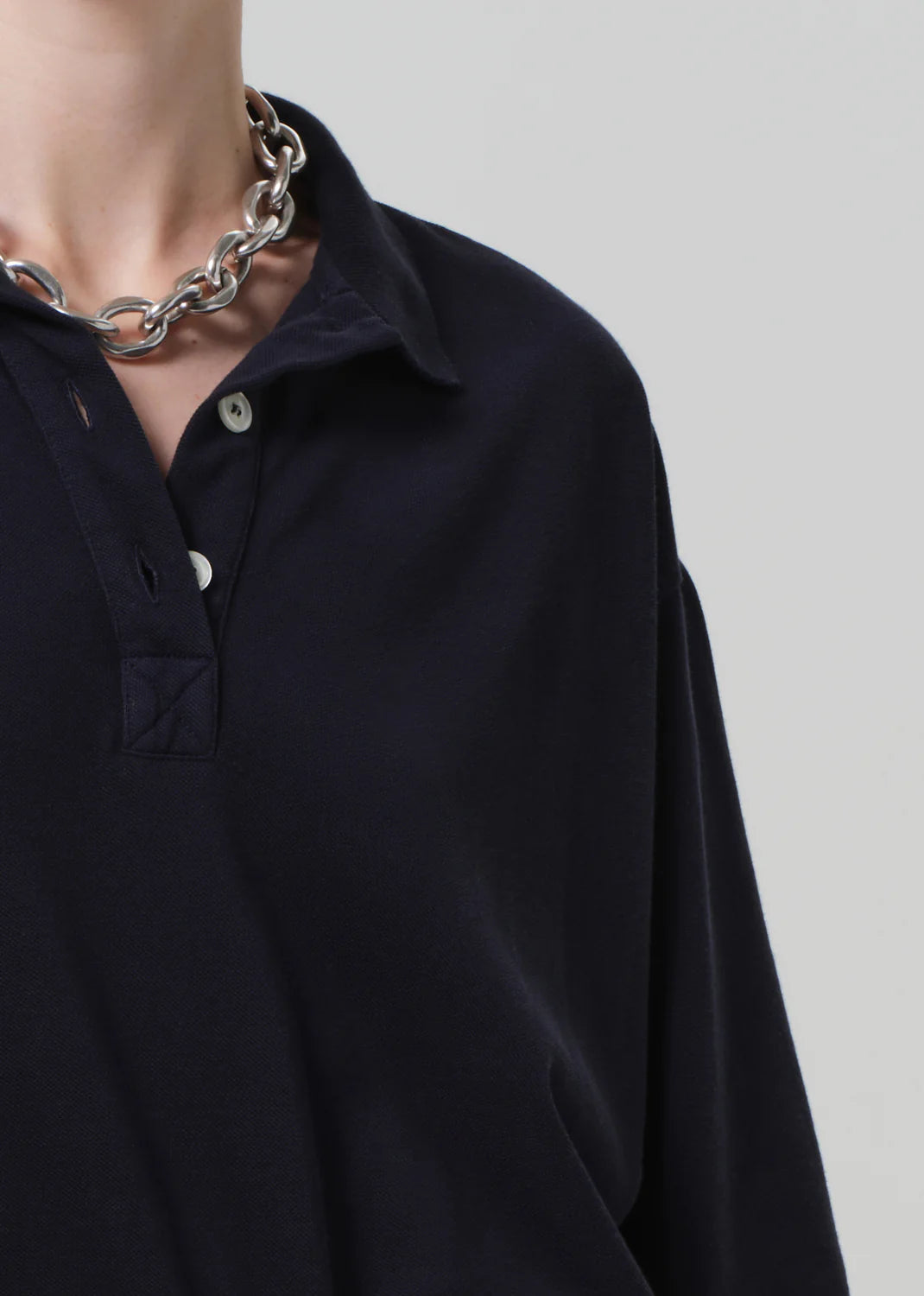 A person wears the Citizens Of Humanity/AGOLDE Lowen Polo Shirt in dark pique fabric, paired with a chunky silver chain necklace, focusing on the upper chest and neck against a plain, light background.