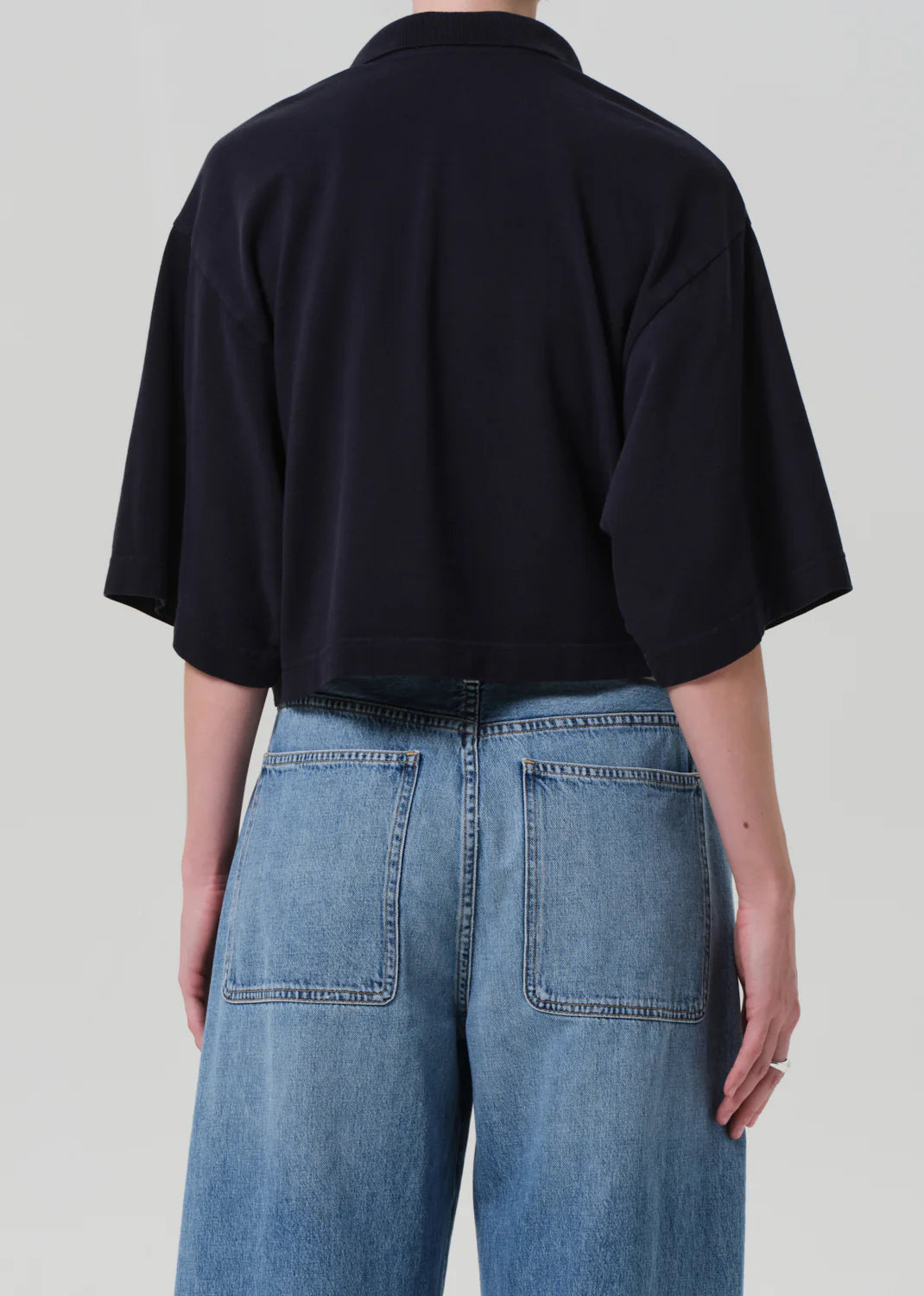 A person is shown from the back against a plain light background wearing the Citizens Of Humanity/AGOLDE Lowen Polo Shirt and high-waisted, light blue denim jeans.