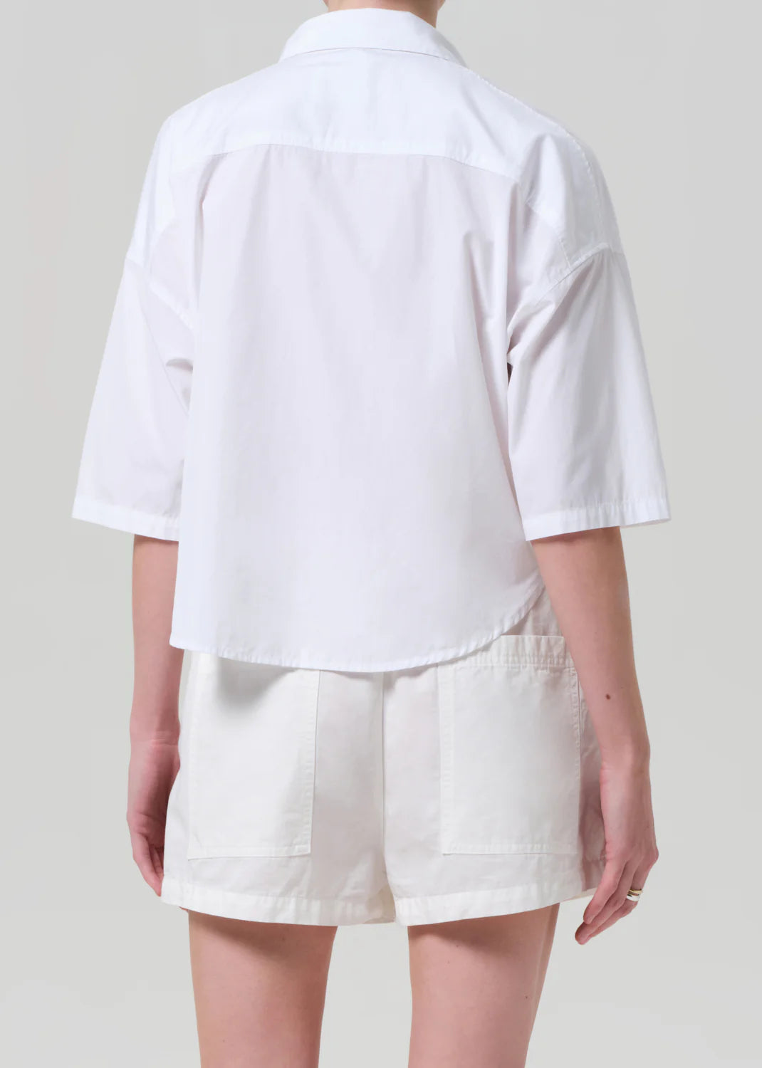 Model shown from the back against a plain, light gray background, wearing the Frances Cropped Cape Button Up by Citizens Of Humanity/AGOLDE and white shorts.