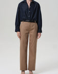 A person wears the Ana Cropped Shirt in Piave by Citizens Of Humanity/AGOLDE, tucked into high-waisted khaki trousers with a black belt, black open-toe sandals, and a delicate necklace, standing against a plain light background.