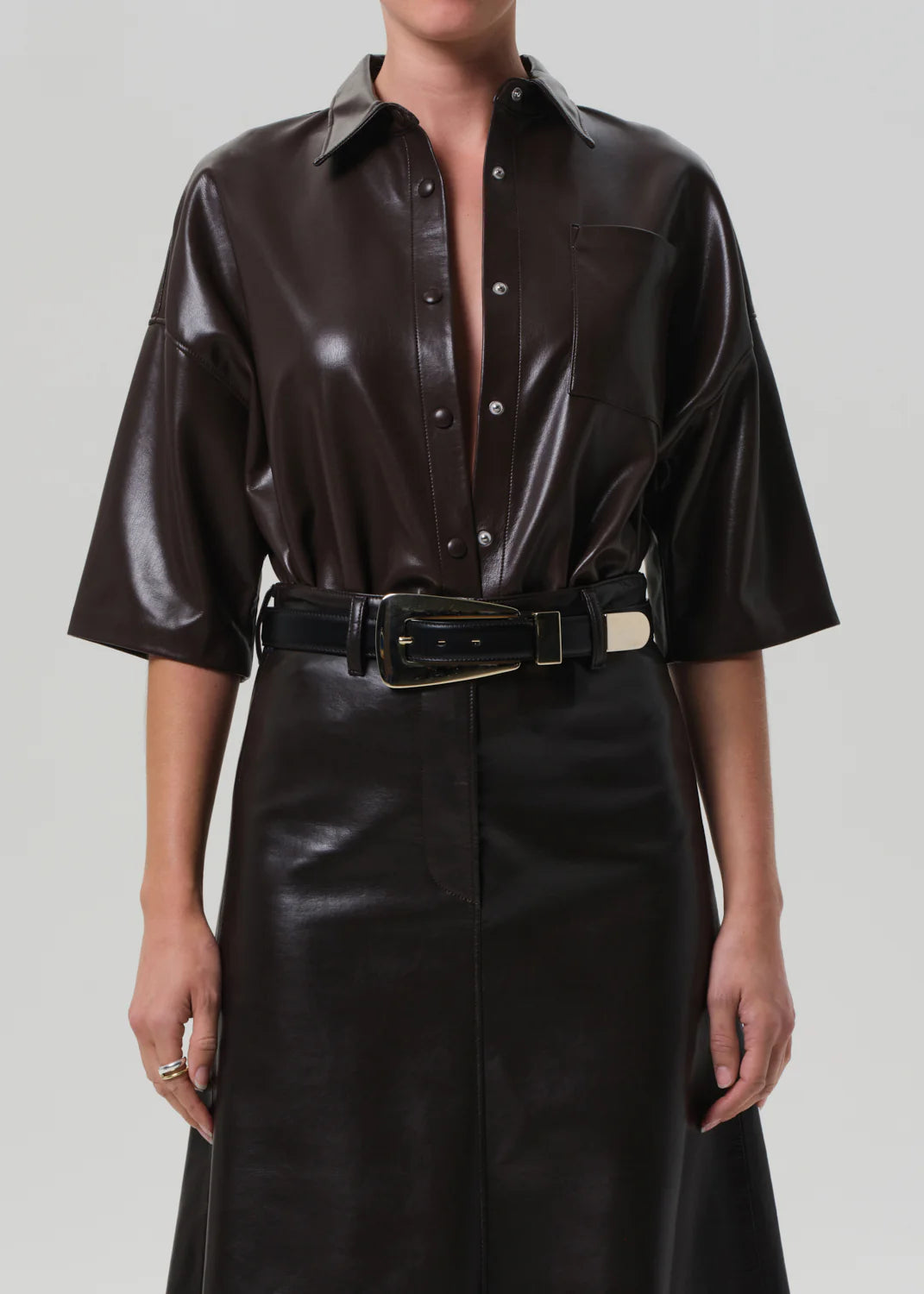 A person wearing the Frances Leather Cropped Cape by Citizens Of Humanity/AGOLDE, styled with a wide black belt featuring a large rectangular gold buckle.
