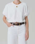 Model wears the gia bubble tee by Citizens Of Humanity/AGOLDE—white cotton, tucked into white jeans with a dark brown belt, gold necklaces, and a ring. Upper body shown against a plain light gray background.