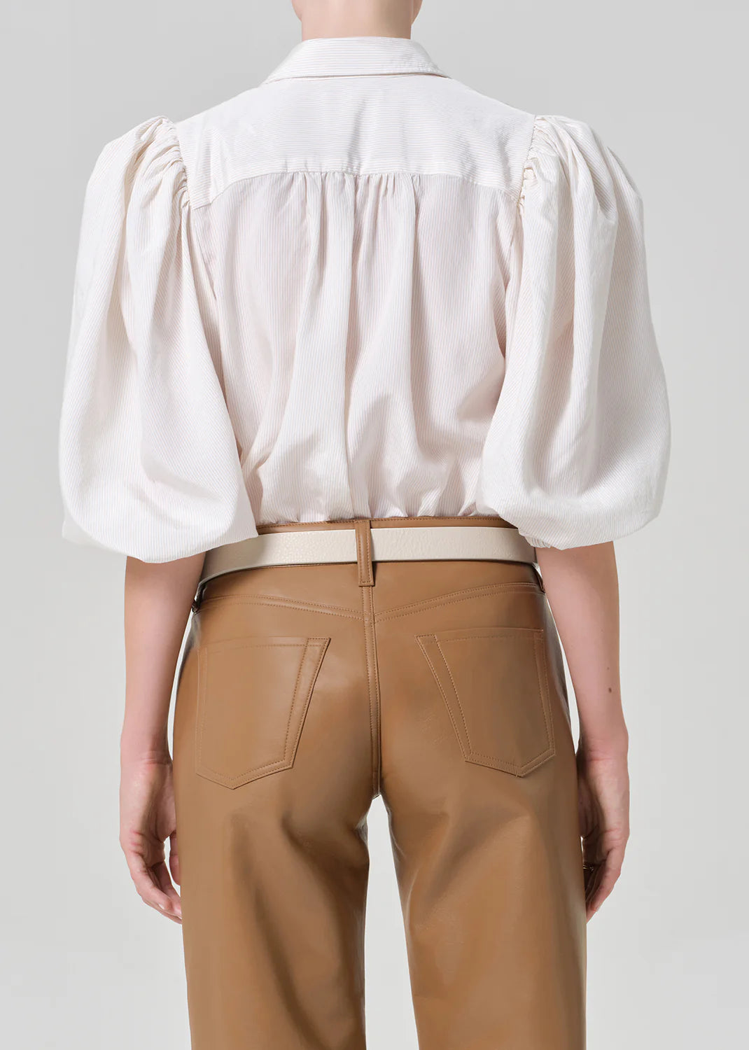 A person seen from behind wears the Anya Puff Sleeve Shirt by Citizens Of Humanity/AGOLDE, styled with tan high-waisted leather pants featuring visible back pockets and a beige belt.