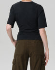 A person faces away from the camera, wearing the Citizens Of Humanity/AGOLDE fabien tee in black with exaggerated sleeves and olive green cargo pants, both set against a plain light gray background.