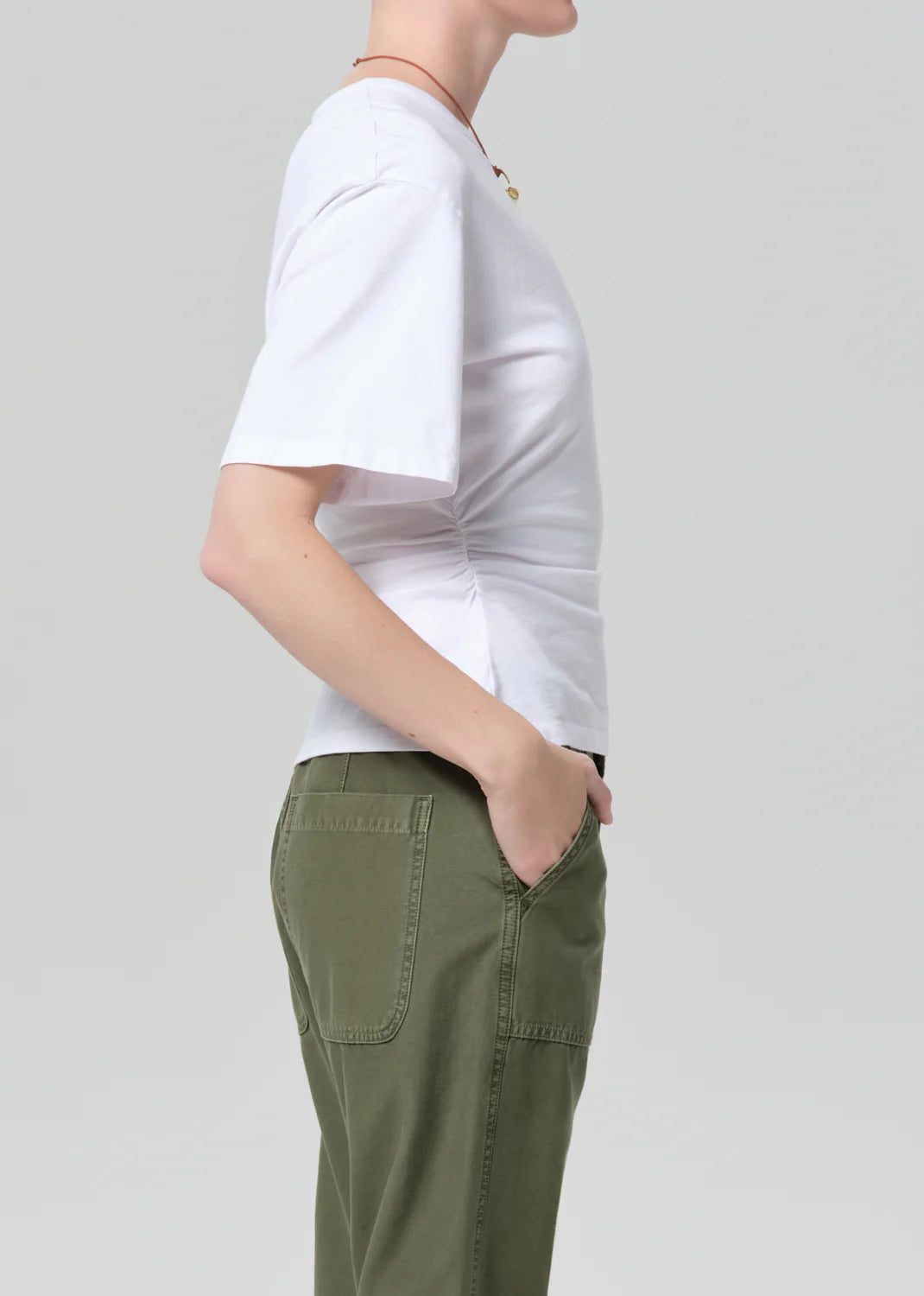 A person in profile wears the fabien tee by Citizens Of Humanity/AGOLDE, featuring exaggerated sleeves, paired with green pants and a necklace against a plain light gray background.