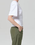 A person in profile wears the fabien tee by Citizens Of Humanity/AGOLDE, featuring exaggerated sleeves, paired with green pants and a necklace against a plain light gray background.