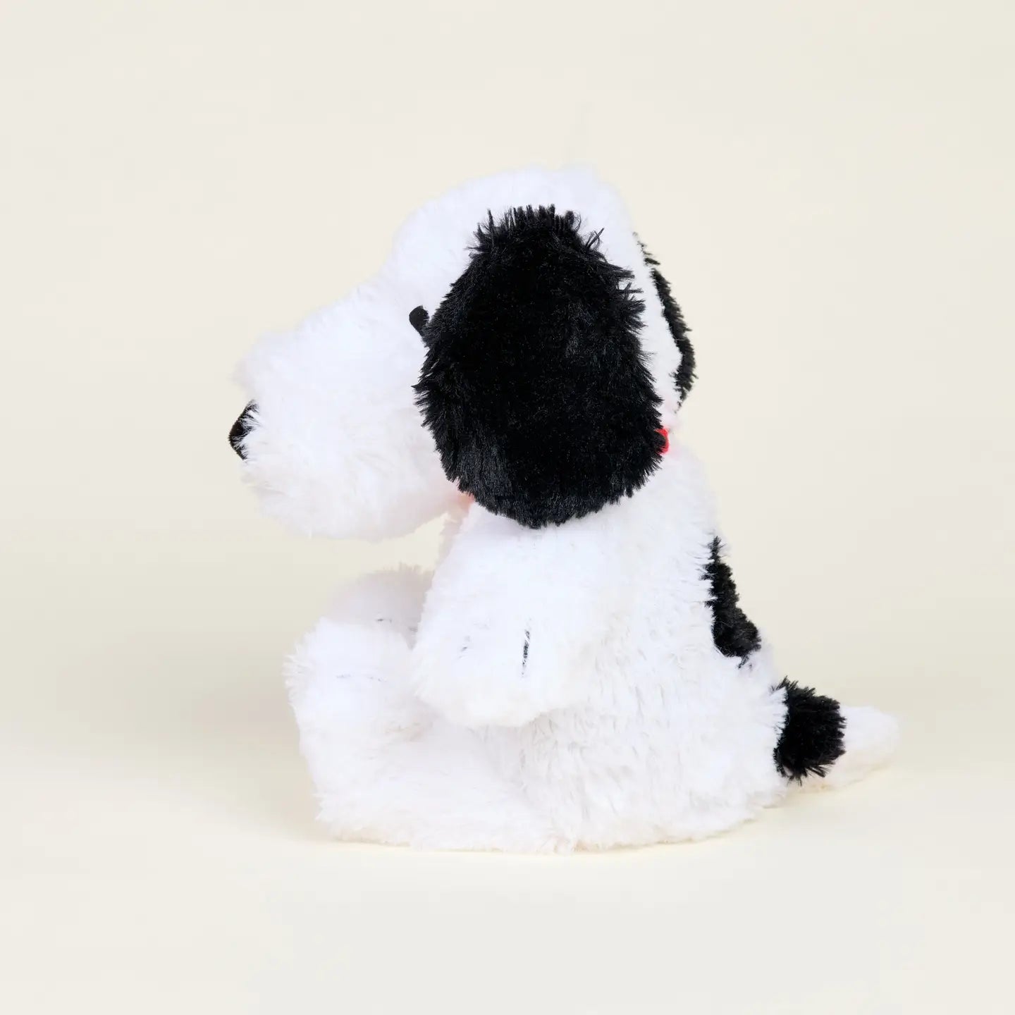 The Snoopy / Red Collar Warmies by Warmies/Intelex is a microwavable plush dog toy in black and white, with floppy black ears, a black nose, and short tail, offering gentle sensory comfort against an off-white background.