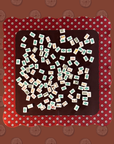 The Faire Wild West Mahjong Mat ONLY features a square shape with a red border and silver studs, covered in mahjong tiles, set on a patterned reddish-brown background—a stylish addition to your game night.