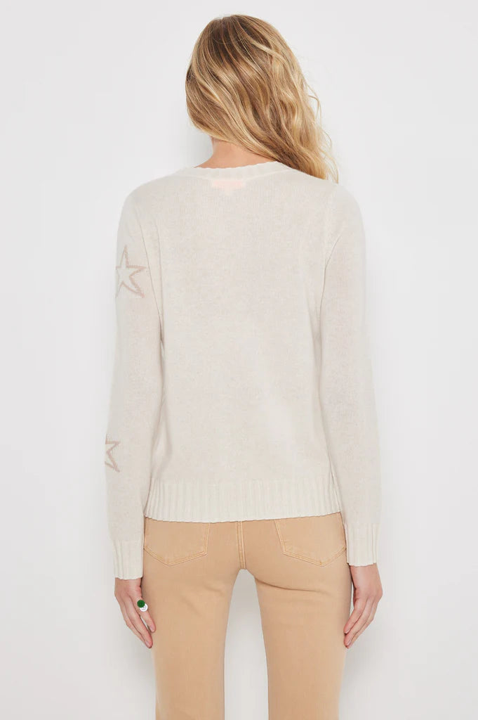 A person with long blonde hair, wearing Lisa Todd's luxurious "Star Dust" cashmere sweater with contrast intarsia stars on the sleeves and beige pants, is seen from the back against a plain white background.