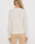 A person with long blonde hair, wearing Lisa Todd's luxurious "Star Dust" cashmere sweater with contrast intarsia stars on the sleeves and beige pants, is seen from the back against a plain white background.