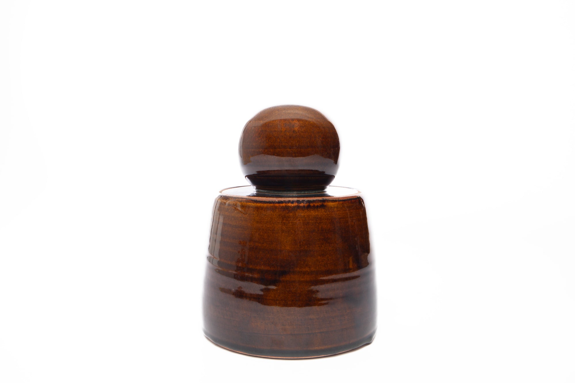 The Faire Amber Stash Jar, a brown ceramic container with a rounded lid reminiscent of hand-thrown stash jars or a small barrel, is shown against a plain white background.