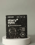 A box of Faire "masks" self-warming eye masks sits on a white pedestal against a gray backdrop. The black packaging with white text and star illustrations features a person wearing an eye mask. It contains five fragrance-free masks.