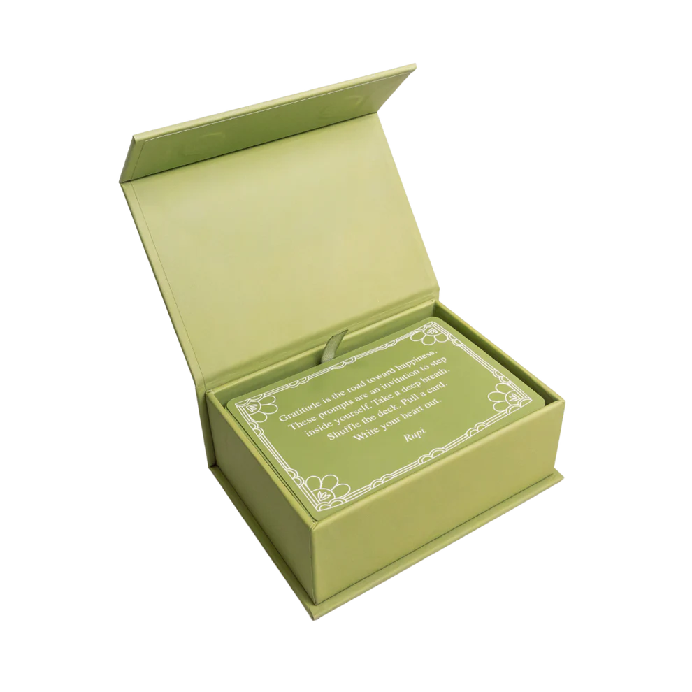 Rupi Kaur's Writing Prompts Gratitude by Simon & Schuster Inc. comes in a light green box with a hinged lid. Inside is a matching card with white borders and printed text, perfect for gratitude journaling. The interior matches the exterior’s green shade.