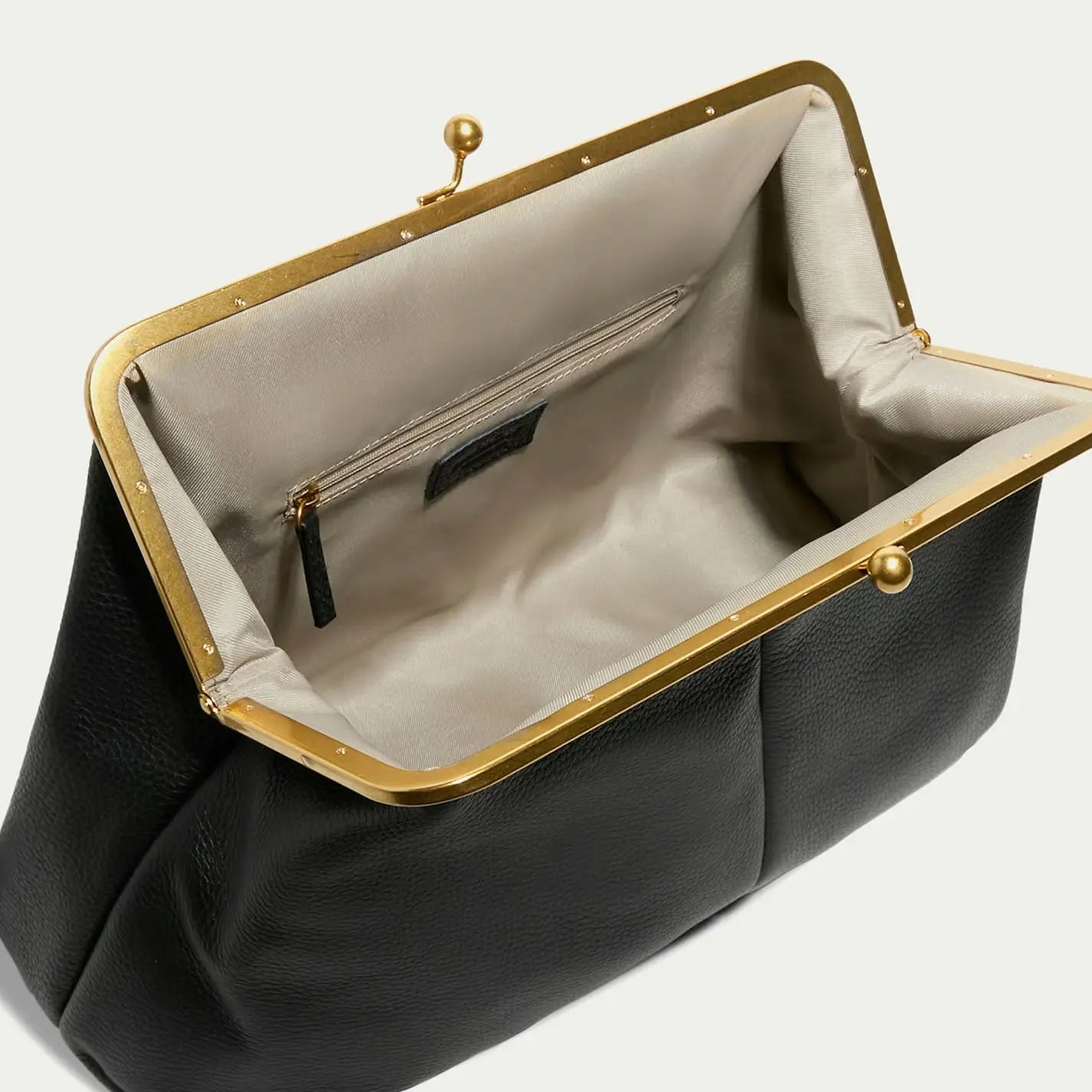 The Grace Oversized Clutch by Faire is a vintage-inspired black leather purse with a gold metal frame and clasp, featuring a beige fabric interior and an inner zippered pocket.