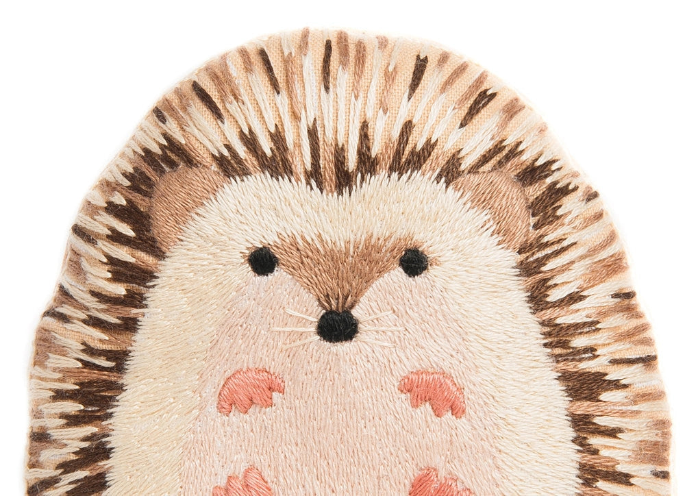 The Hedgehog Embroidery Kit by Faire features a cute hedgehog with brown and tan quills, round eyes, dark nose, and pink feet on a white background—ideal for DIY projects or as a charming pattern.
