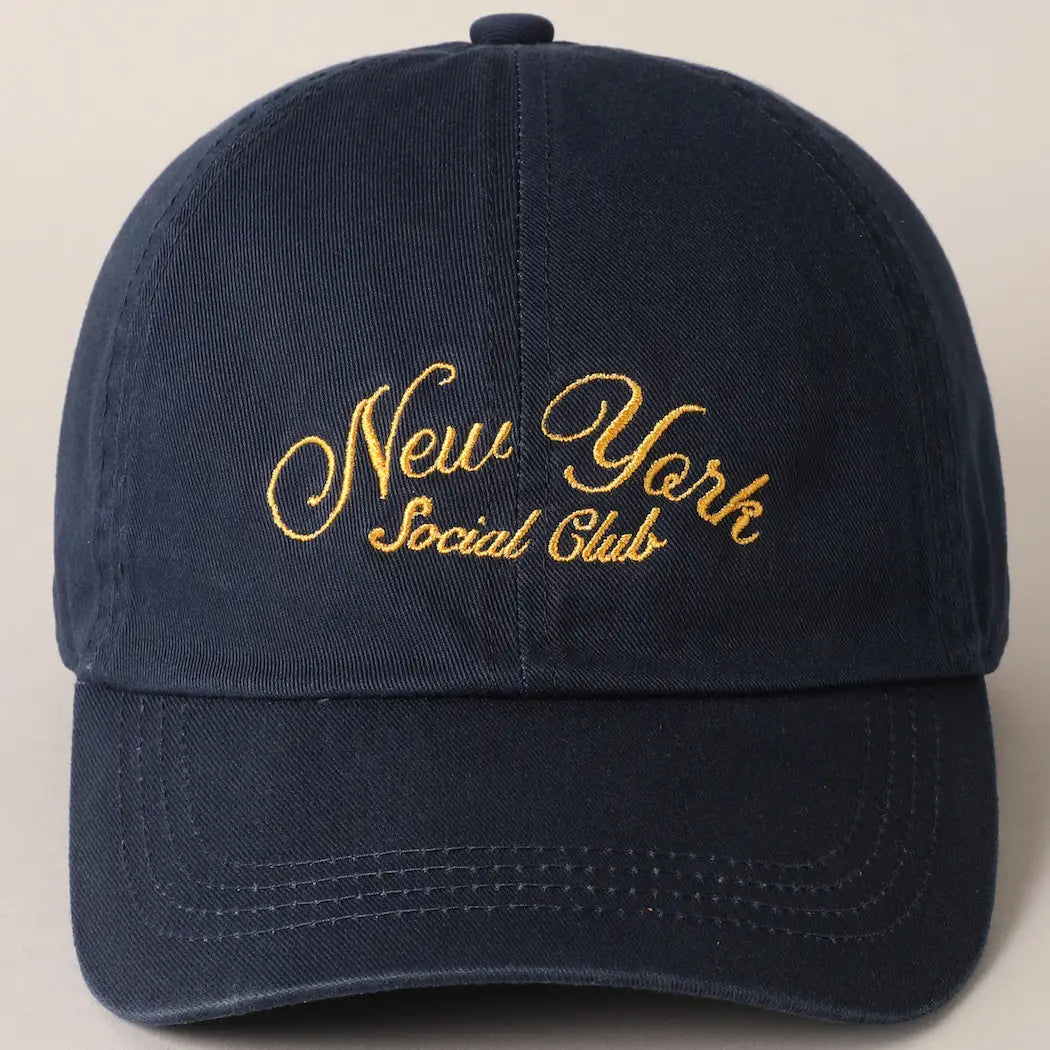 The Faire New York Social Club Baseball Cap in navy blue has "New York Social Club" embroidered in yellow cursive on the front and features an adjustable strap.