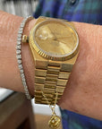 A wrist adorned with a dazzling watch from Lucky Star, featuring gold Watch/Bag Charms and a small pendant. The watch showcases a stunning gold band and face, perfectly matched with a silver bracelet inlaid with gemstones. This elegant ensemble is highlighted by the person's blue and green plaid shirt, making it an ideal gifting option.