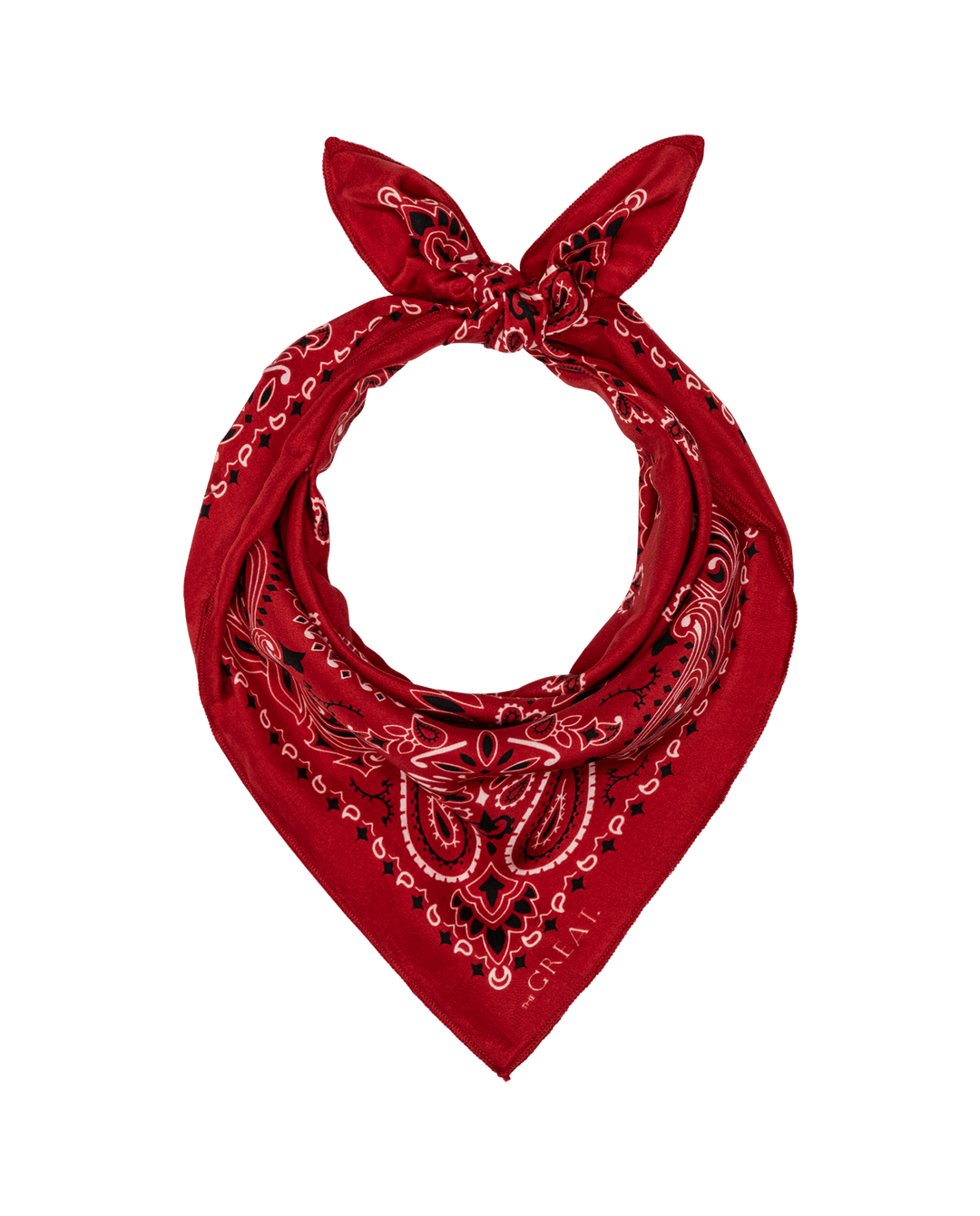 The Silk Bandana by The Great Inc. is a red silk accessory featuring a white and black paisley pattern, folded and knotted at the top for a timeless, vintage-inspired look.
