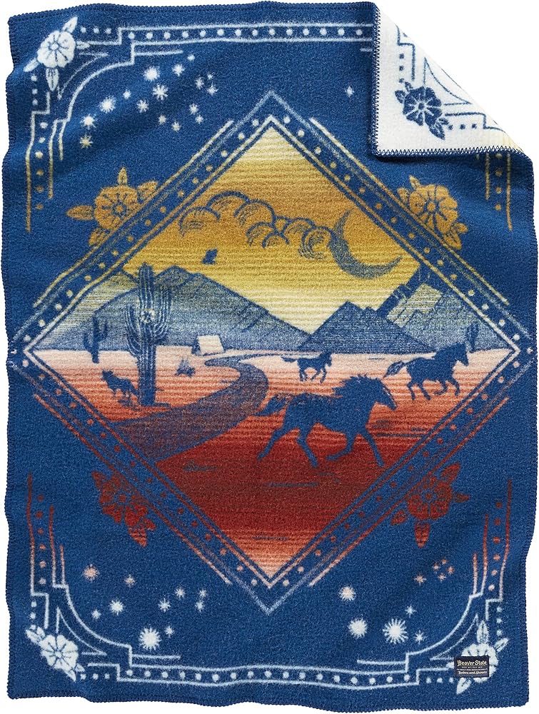 The Jacquard Whipstitch Muchacho by Pendleton/Babbitt's Wholesale is a pure virgin wool woven blanket featuring a desert scene with horses, cacti, mountains, and clouds in a diamond frame, plus blue, white, orange, and yellow floral/star borders.