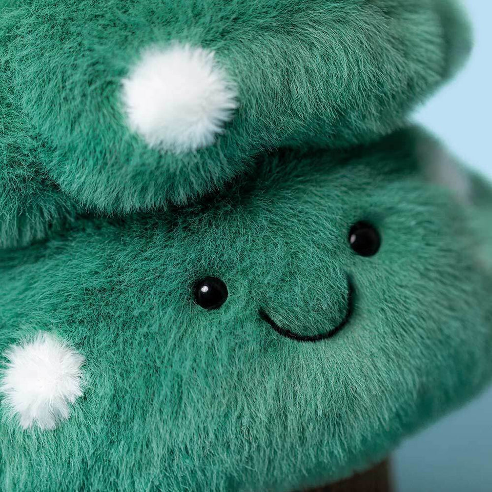 Close-up of the Jelly Cat Inc. Amuseables Christmas Tree plush, shaped like a bush with white fluffy spots, black bead eyes, and a stitched smile on a light blue background—perfect festive decor!.