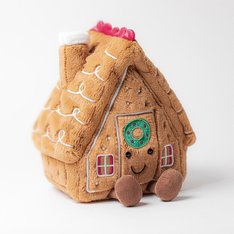 The Amuseables Gingerbread House by Jelly Cat Inc. is a plush toy with stitched decorations, a smiling face on the door, and two soft brown feet, shown against a plain white background.