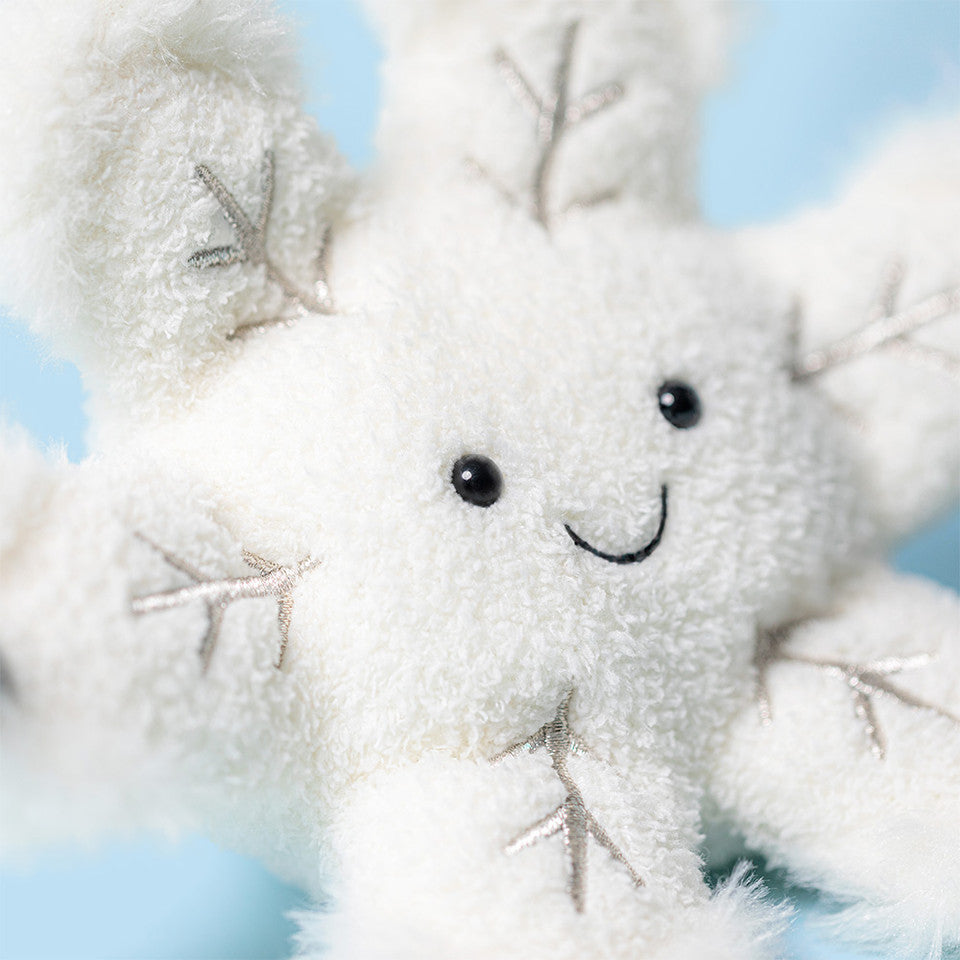 The Amuseable Snowflake by Jelly Cat Inc. is a soft, plush toy featuring embroidered silver branches, black button eyes, and a smiling mouth—perfect for adding charm to any light blue setting.