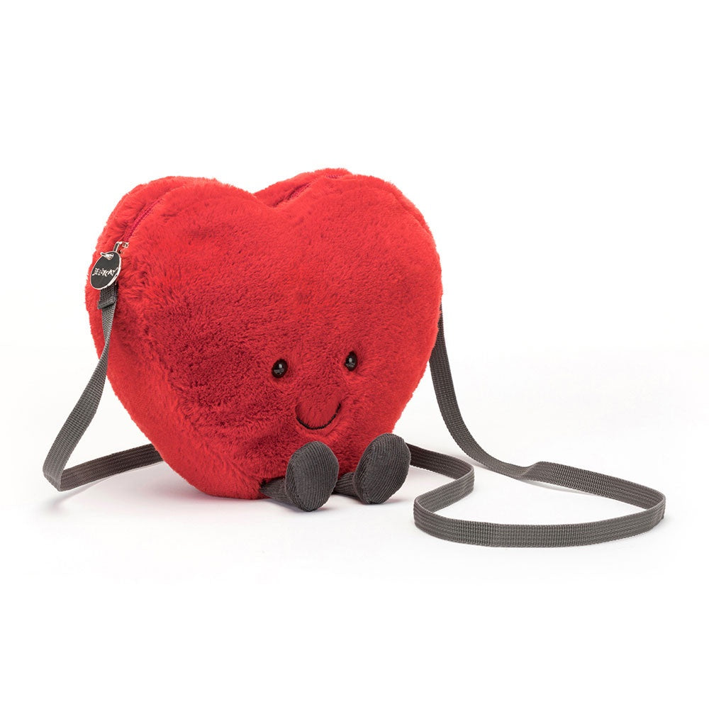 The Amuseables Heart Bag by Jelly Cat Inc. is a playful, soft scarlet fur heart-shaped bag with a smiling face and tiny black shoes. It features a long cross-body strap for easy carrying, making it an undeniably cute and cheerful addition to any outfit.