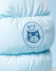 Close-up of the Jelly Cat Inc. Amuseables Mitten light blue puffy jacket featuring an embroidered cartoon cat face with stacked hats and a mitten, set in a circle on a soft blue background.