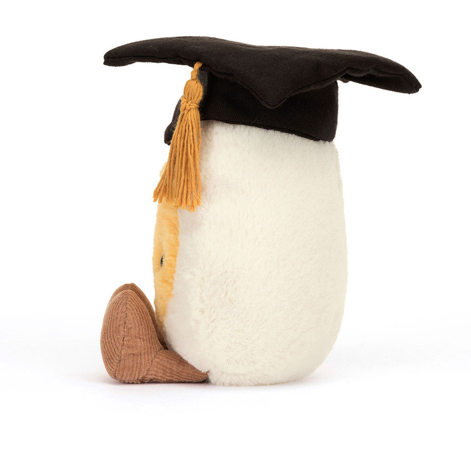 The Amuseables Boiled Egg Graduation by Jelly Cat Inc. sits upright against a white background, featuring super-soft fur and proudly wearing a cotton mortarboard with a yellow tassel.
