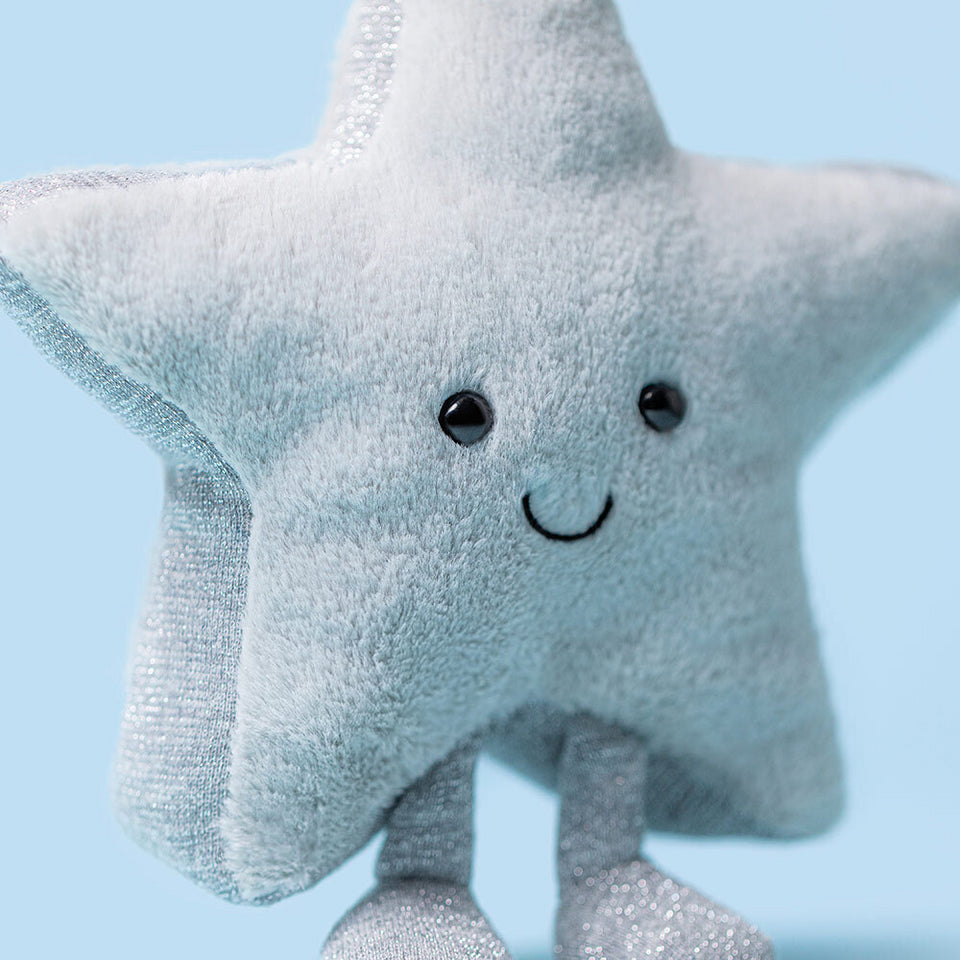 The Amuseables Silver Star by Jelly Cat Inc. is a soft plush toy featuring a smiling face, black button eyes, and glittery silver legs—perfect for any dreamer and displayed against a light blue background.