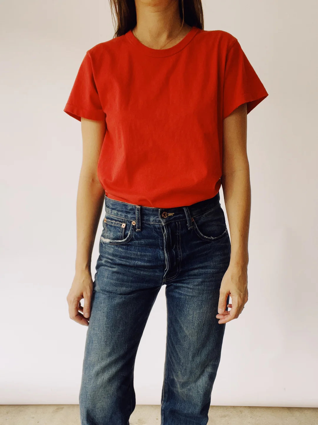 A person wearing "The Crew," a vintage fit T-shirt in red by Hey Gang, along with blue jeans, stands against a plain white background.