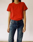 A person wearing "The Crew," a vintage fit T-shirt in red by Hey Gang, along with blue jeans, stands against a plain white background.