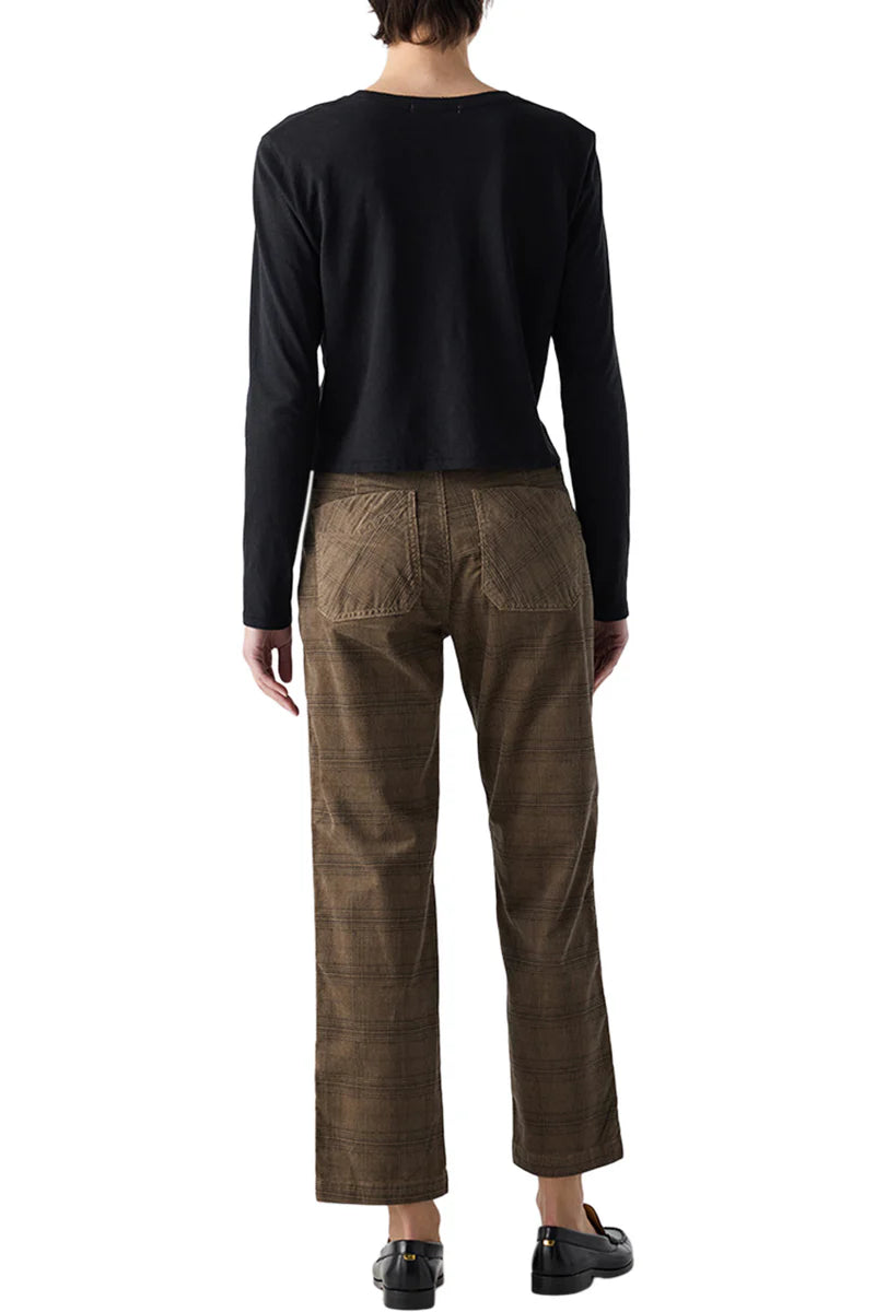 A person stands facing away against a white background, wearing AMO Denim's Lillian Plaid Cord straight-leg pants with a long-sleeve black top and black shoes.