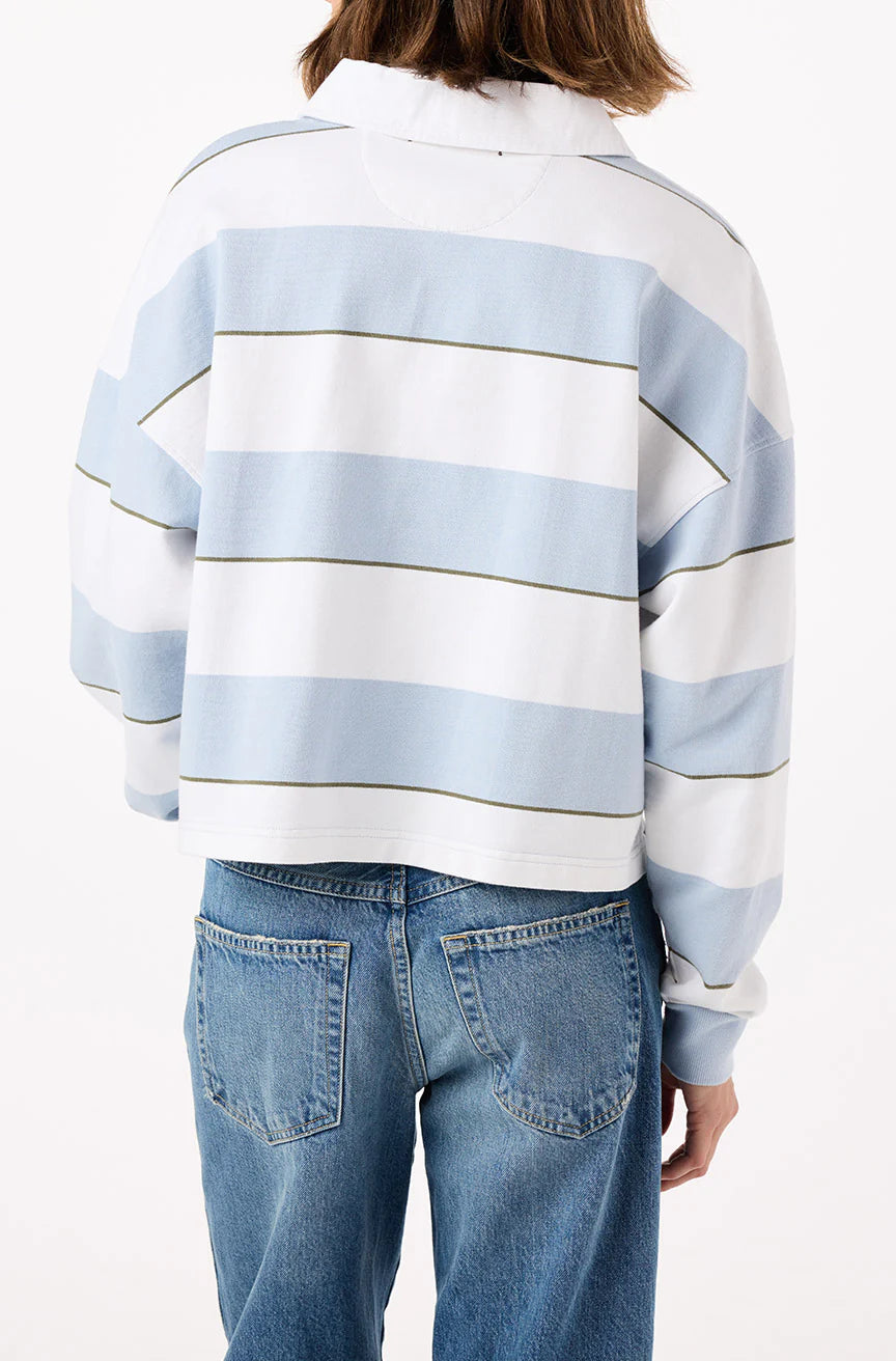 A person wearing the Crop Annie Rugby, a blue and white striped crop top from AMO Denim, is photographed from the back. The long-sleeved sweater's wide horizontal stripes pair well with their medium-length brown hair and blue jeans.