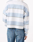 A person wearing the Crop Annie Rugby, a blue and white striped crop top from AMO Denim, is photographed from the back. The long-sleeved sweater's wide horizontal stripes pair well with their medium-length brown hair and blue jeans.