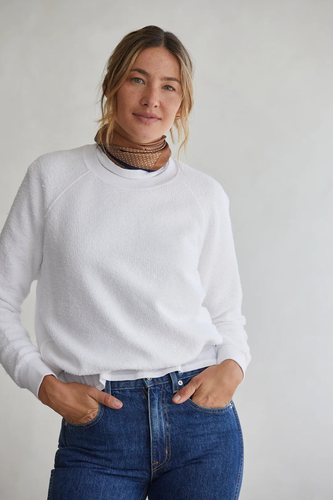 A person with long hair is wearing the Perfectwhitetee Ziggy Inside Out LS Crewneck Sweatshirt paired with blue jeans and a layered necklace. They pose confidently with their hands in pockets against a neutral background, embodying the vibe of a cozy essential.