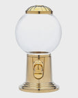 The Godinger (Faire) Candy Machine is a gold-toned candy dispenser that boasts a clear, round glass globe at the top and a gold lever for dispensing at the front. Its base features durable construction and complements the gold accents on the globe's top. This nostalgic piece is showcased against a plain white background.