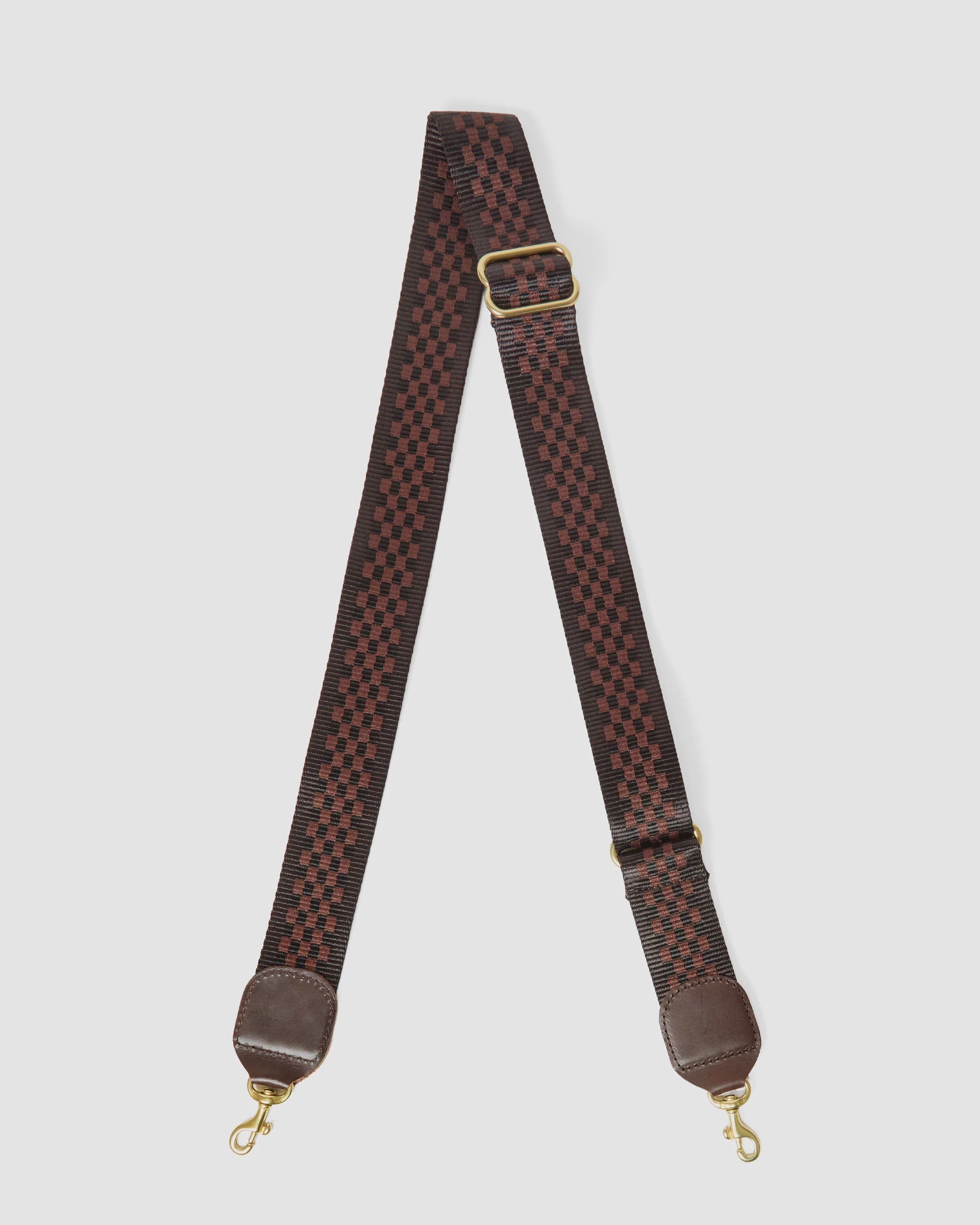 The Clare Vivier Crossbody Strap 26 features red and black checkered nylon webbing, brown leather ends, brass snap hooks, and an adjustable gold buckle. Shown on a white background.