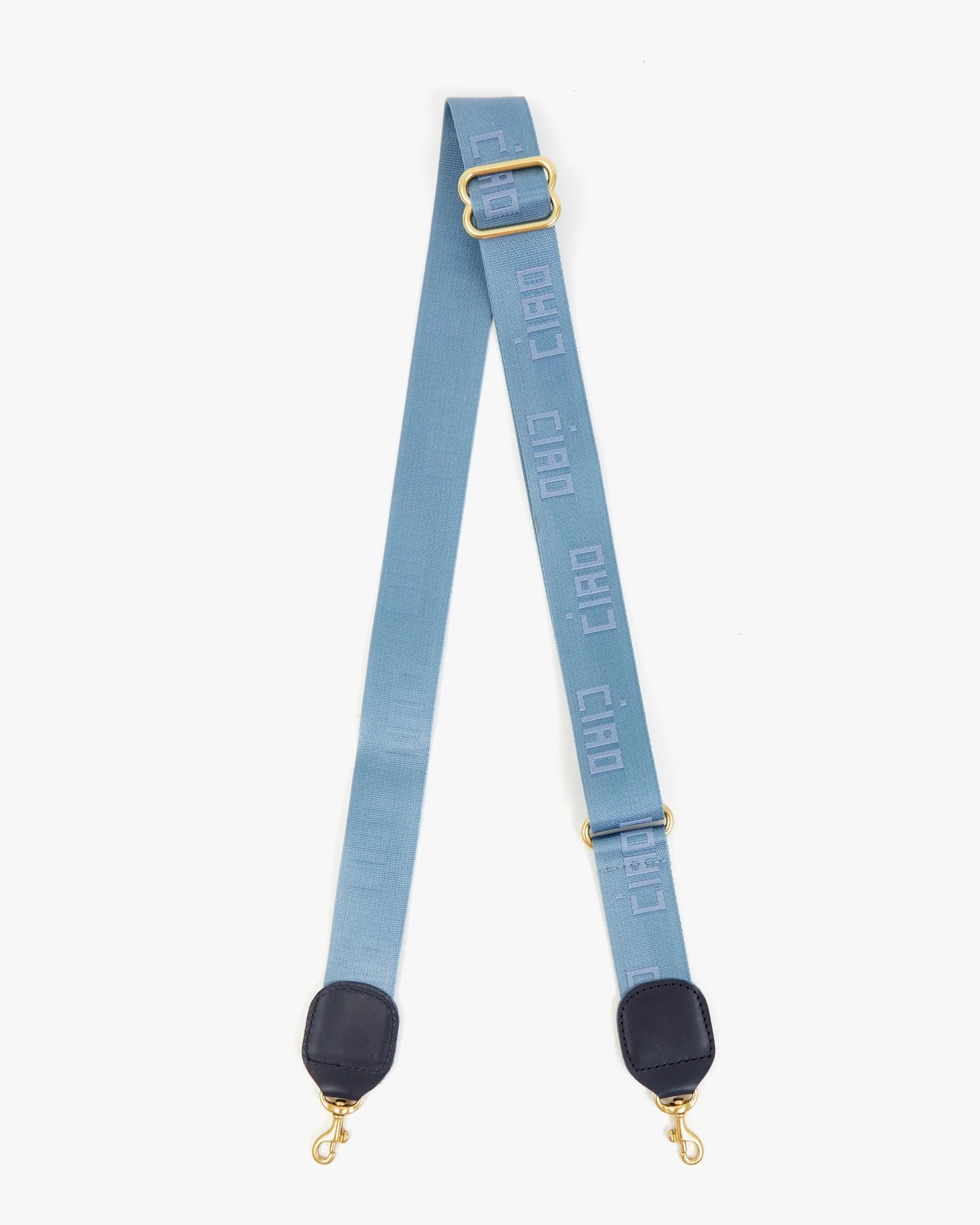 The Clare Vivier Adjustable Crossbody Strap features light blue cotton webbing, gold clips, black leather ends, and "CIAO" printed in white along the length.